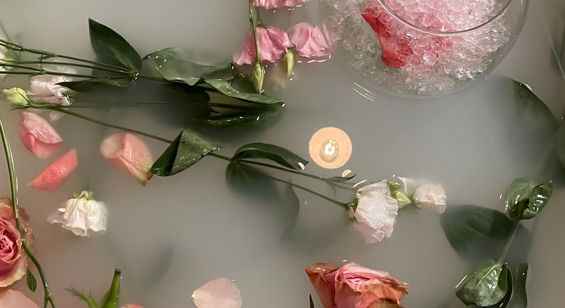 Various pink and white flowers floating on the surface of water with a bowl of ice nearby.
