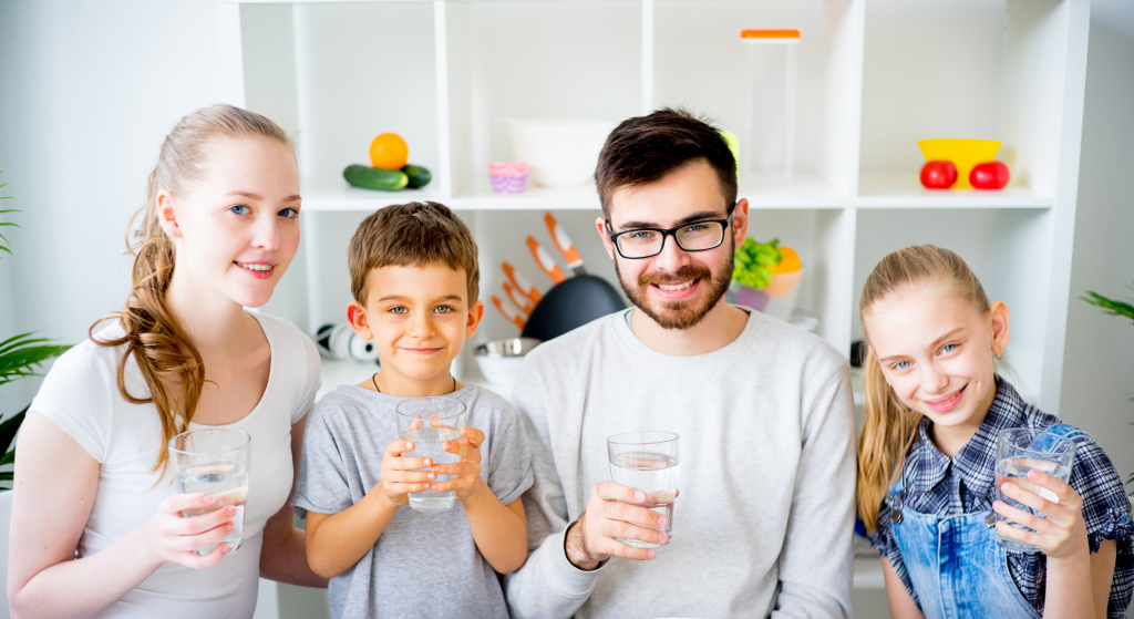 Four individuals, two adults and two children, holding glasses of water while smiling at the camera.