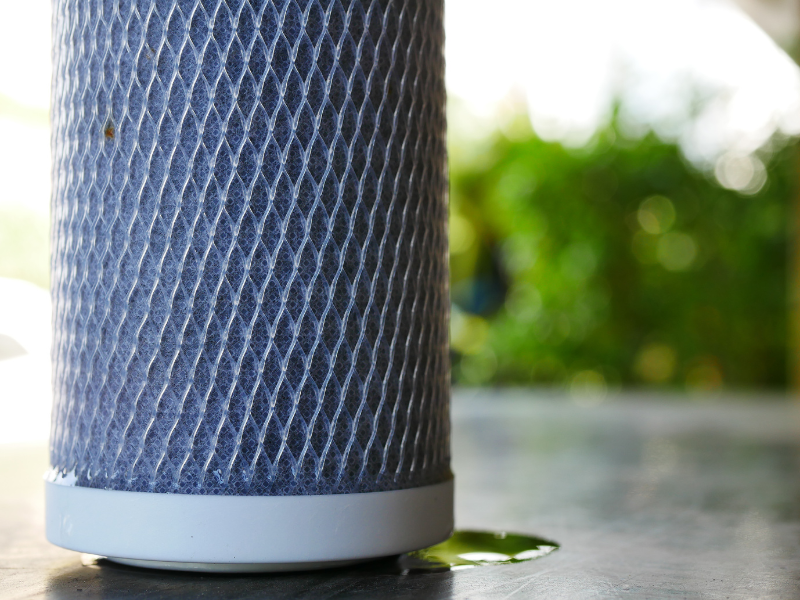 Close-up of a cylindrical water filter cartridge with a textured surface and a small puddle of water underneath.
